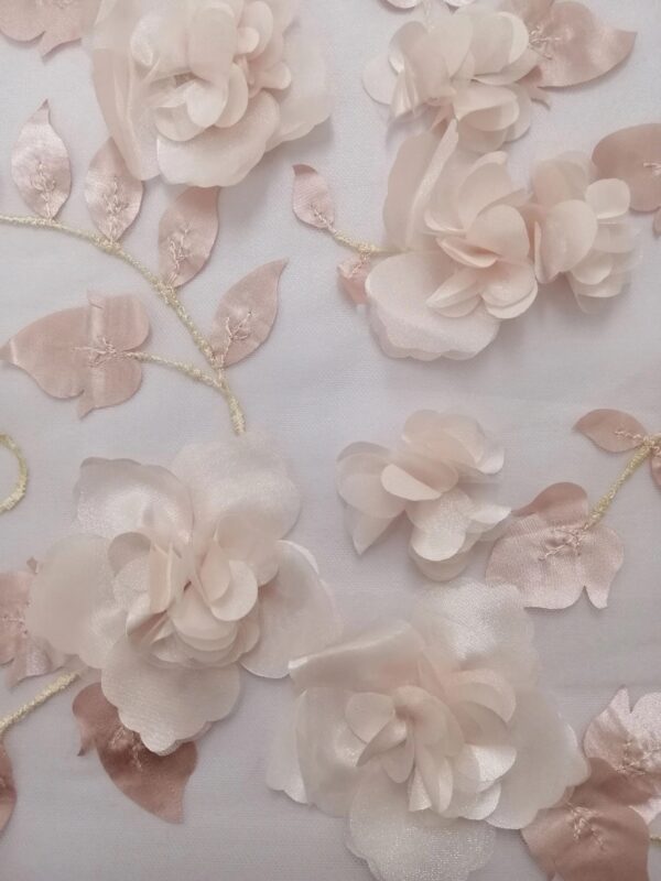 A photo of the veil laid flat on a white surface. The veil is in the pink color. The leafs have a slight shine to them and reflect a light but dusty pink color. The satin and organza petals have a light ballet pink color. The organza petals have a slight sparkle to them. Lastly the stems that have been embroidered into the pale ivory tulle base and are a light gold ivory color. In the photo you can see several of the different sizes of flowers and leafs.